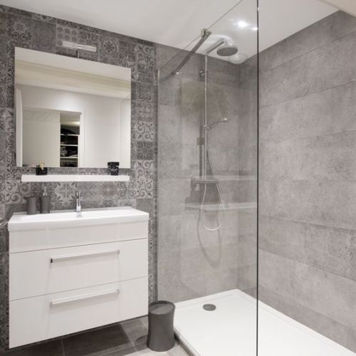 Baño con azulejos en tono gris, plato de ducha y sanitarios de color blanco